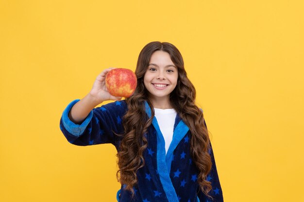 Gelukkig kindmeisje geniet van het ochtendontbijt van verse appel in een gezellige biologische badjas