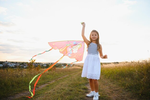 Gelukkig kindmeisje met een vlieger die op weide in de zomer in aard loopt