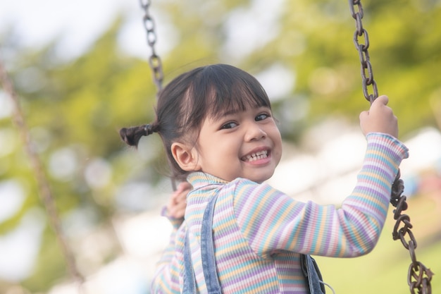 Gelukkig klein Aziatisch meisje dat buiten in het park schommelt
