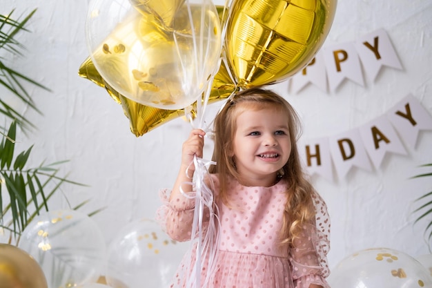 Gelukkig klein blond meisje in roze jurk met ballonnen en viert haar verjaardag