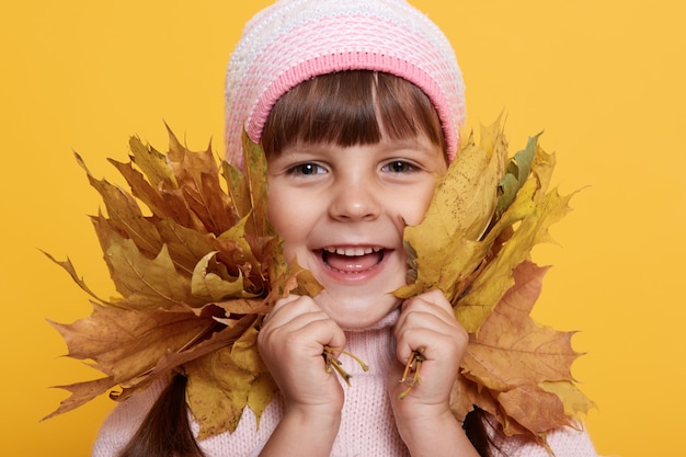 Gelukkig klein kind, babymeisje lachen en spelen met Herfstbladeren, kijkt naar voorzijde met charmante glimlach,