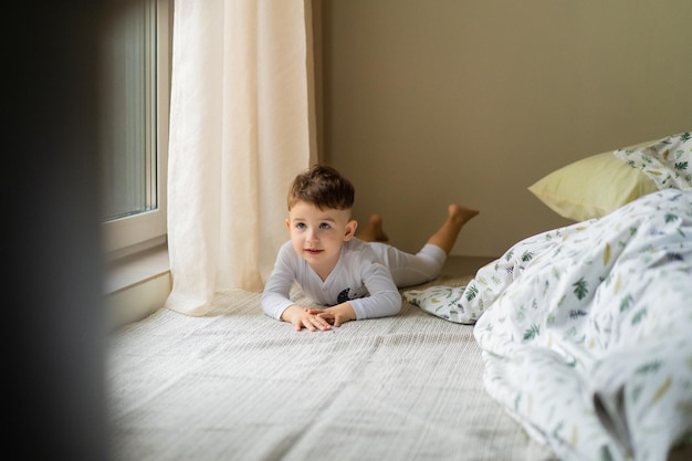 Gelukkig klein kindjongen in pyjama, in bed in de slaapkamer met speelgoed, speelt, slaapt. Prachtig babybed. Slaap overdag voor kinderen. Zacht licht.