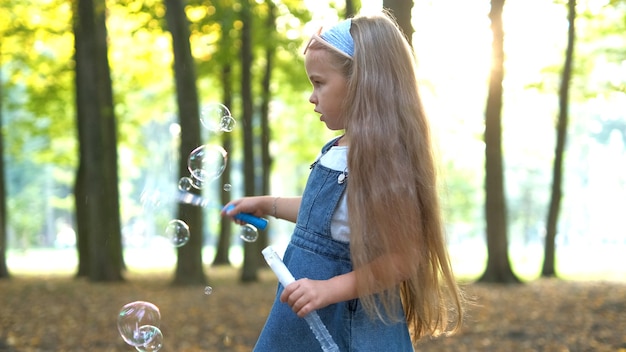 Gelukkig klein kindmeisje die zeepbellen buiten in groen park blazen. Outdoor zomeractiviteiten voor kinderen concept.