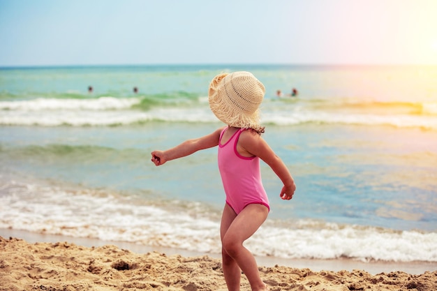 Gelukkig klein meisje dat in de zomer op het strand loopt het meisje kijkt terug kind in een strohoed