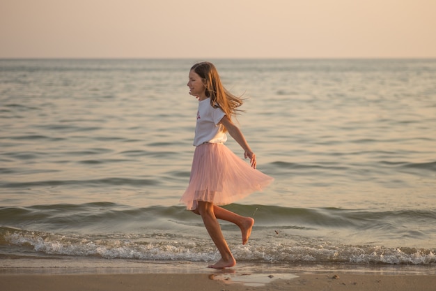 Gelukkig klein meisje draait en danst op het strand op een zonnige dag.