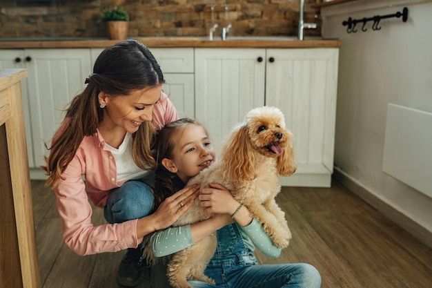 Gelukkig klein meisje en haar moeder genieten met hun hond thuis.