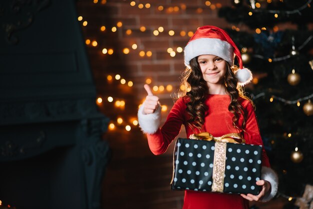 Gelukkig klein meisje glimlachend met geschenkdoos in de buurt van de kerstboom. Kerstconcept.