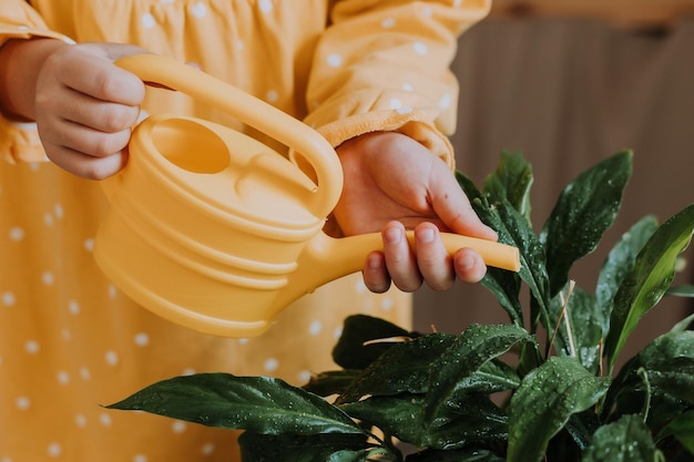 gelukkig klein meisje in een gele katoenen jurk geeft bloemen water in de datsja. houten veranda