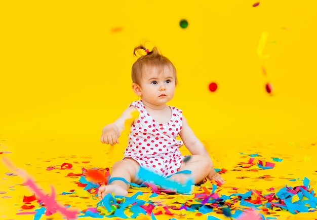 Gelukkig klein meisje in een jurk in erwten vangt confetti op een gele achtergrond. plaats voor tekst