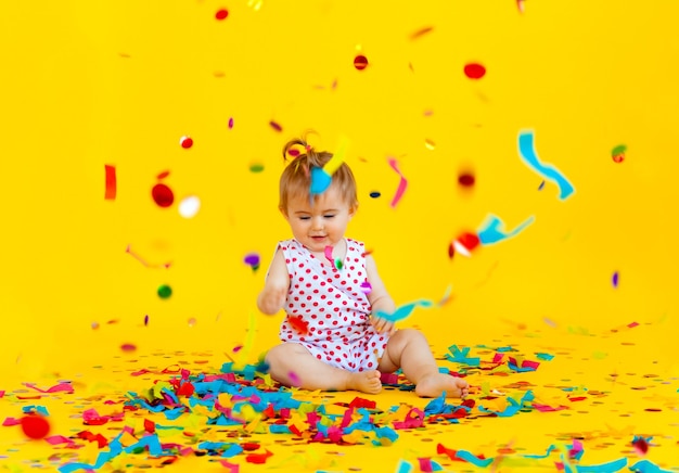 Gelukkig klein meisje in een jurk in erwten vangt confetti op een gele achtergrond. plaats voor tekst