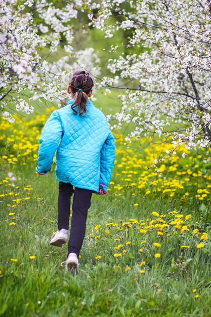 Gelukkig klein meisje in een lentetuin met bloeiende kersenbomen