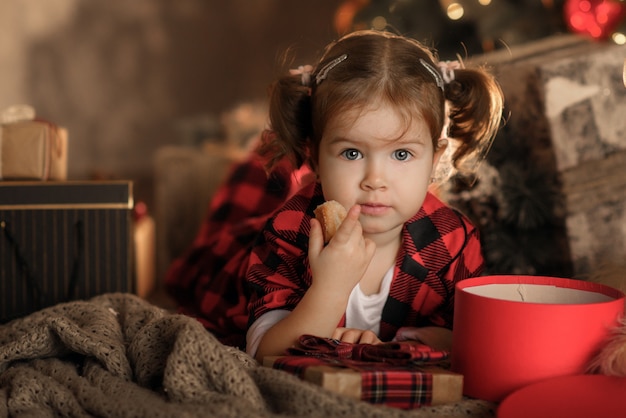 Gelukkig klein meisje in rode pyjama's en kerstmuts met kerst geschenkdoos in de woonkamer