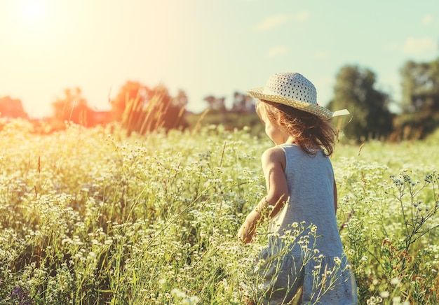 Gelukkig klein meisje in strohoed wandelen in het bloemenveld op een zonnige zomerdag