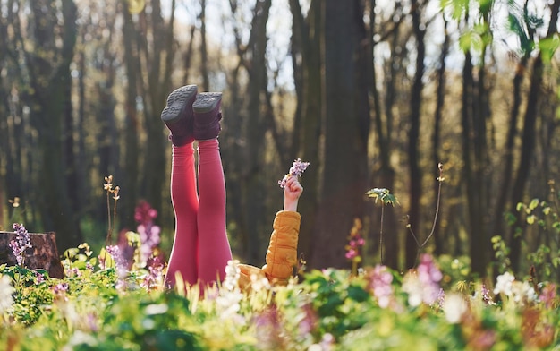 Gelukkig klein meisje in vrijetijdskleding die overdag op de grond in het lentebos ligt