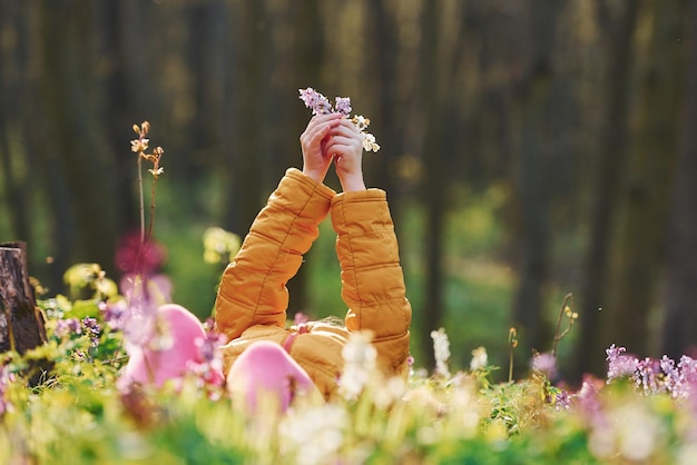 Gelukkig klein meisje in vrijetijdskleding die overdag op de grond in het lentebos ligt