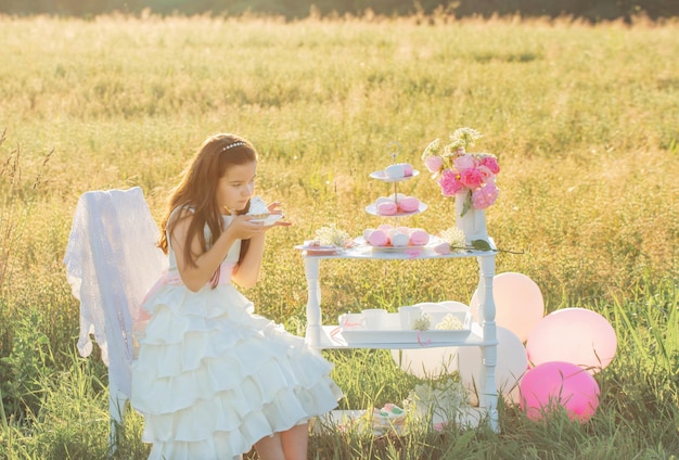 Gelukkig klein meisje in witte jurk met verjaardagstaart in zomer veld