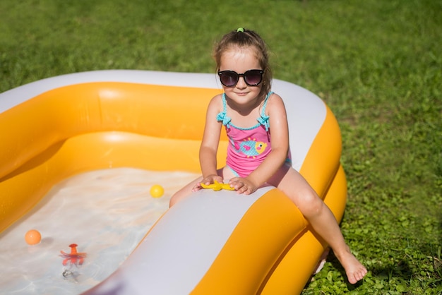 Gelukkig klein meisje in zwembroek spelen in het opblaasbare zwembad in zonnige dag