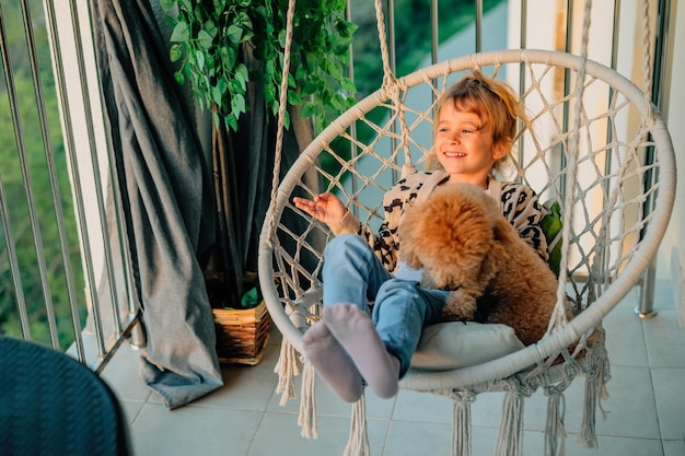 Gelukkig klein meisje knuffelt met een glimlach haar poedelhond thuis op het balkon in het voorjaar