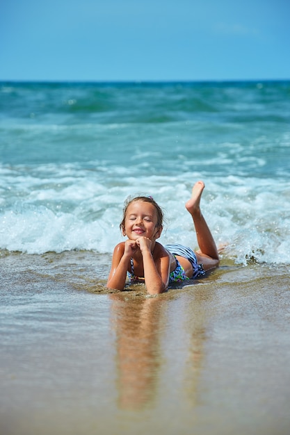 Gelukkig klein meisje ligt aan de kust in de golven tijdens de zomervakantie op het strand, kind, kind spelen aan zee, zomertijd, resot vakantie.