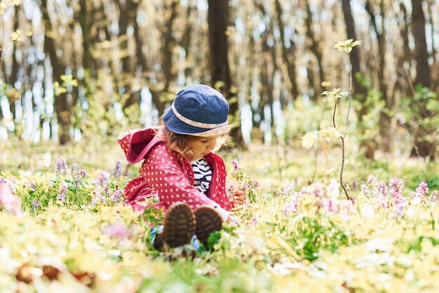 Gelukkig klein meisje met blauwe hoed heeft overdag een wandeling in het lentebos