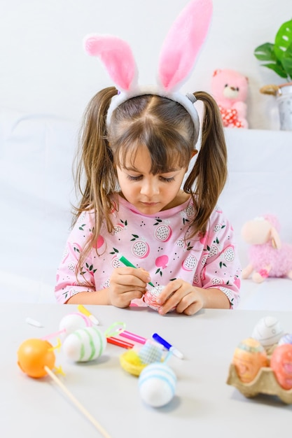 Gelukkig klein meisje met konijnenoren die het ei schilderen met fiberpen en zich voorbereiden op Gelukkige Paasdag