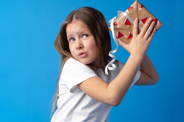 Gelukkig klein meisje met lang haar met een geschenkdoos op een blauwe achtergrond