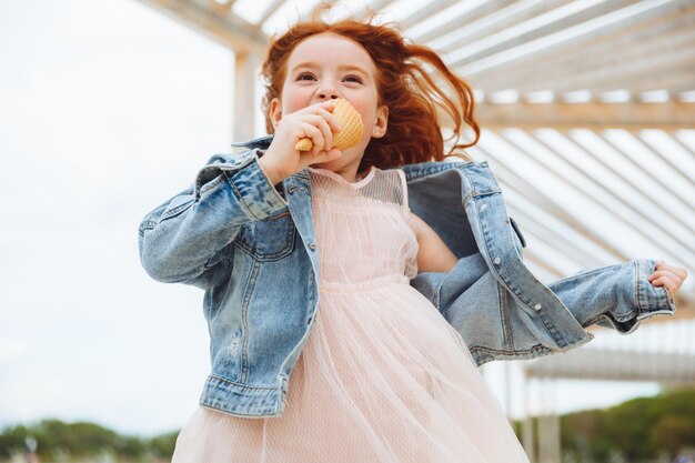 Gelukkig klein meisje met rood haar eet ijs op het strand in de zomervakantie