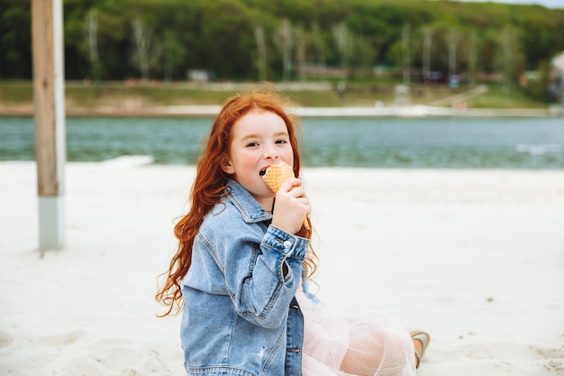 Gelukkig klein meisje met rood haar eet ijs op het strand in de zomervakantie