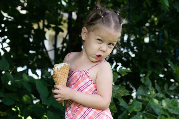 Gelukkig klein meisje met wafelhoorn van ijs kijkend naar camera in het zomerpark