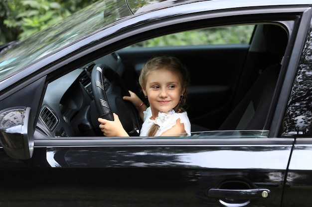 Gelukkig klein meisje zit achter het stuur van papa's auto. Het concept van geluk