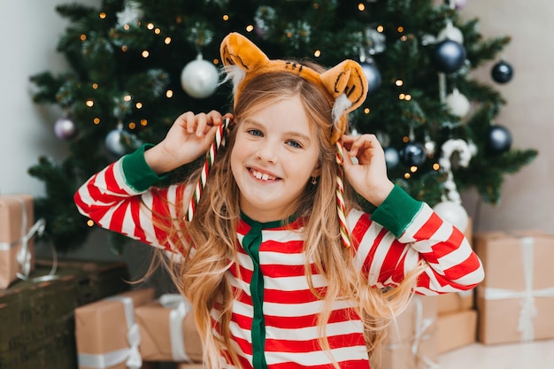 Gelukkig klein meisje zit met snoep in de buurt van de kerstboom. Kerstmis.