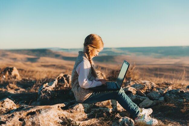 Gelukkig klein tienermeisje zit op een heuvel met een laptop. Digitale nomaden