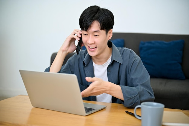 Gelukkig knappe Aziatische mannelijke freelancer praten aan de telefoon met zijn klant werk vanuit huis