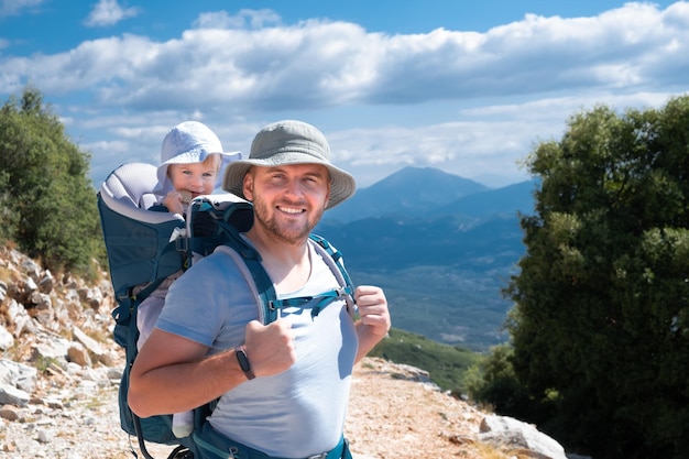 Gelukkig knappe blanke manvader met rugzak met babypeuter met zonnehoed reizen in de natuur in zonnig zomerweer camera kijken Familie met kind wandelentrekking