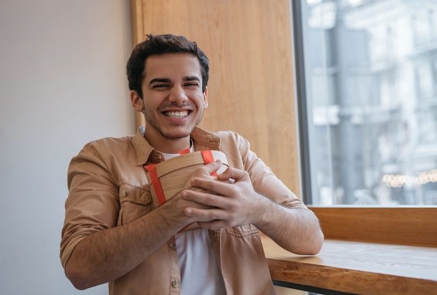 Gelukkig knappe Indiase man met geschenkdoos camera kijken