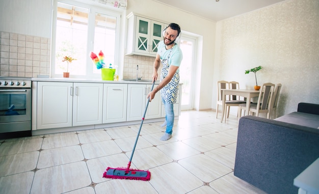 Gelukkig knappe jonge baard man is het schoonmaken van de vloer in de binnenlandse keuken en veel plezier.