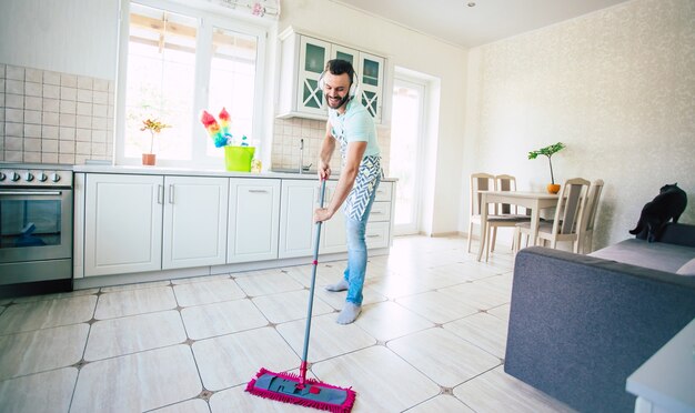 Gelukkig knappe jonge baard man is het schoonmaken van de vloer in de binnenlandse keuken en veel plezier.