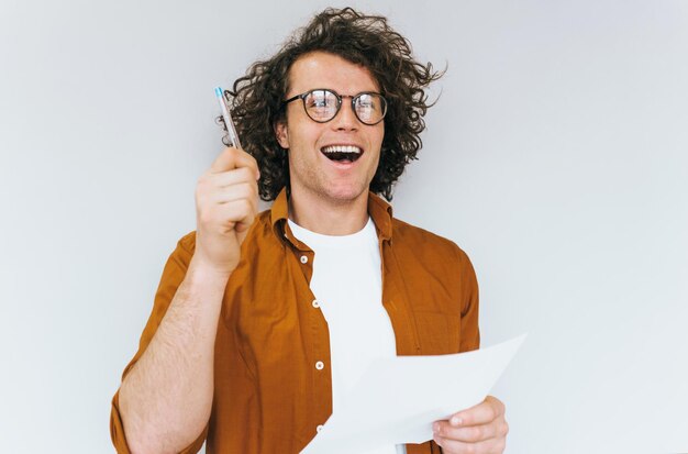 Gelukkig knappe verkoper met krullend haar schrijft op papier voor nieuwe plannen voor zaken poseren over witte studio muur Glimlachende manager man draagt ronde bril maakt notities in notitieboekje voor verkooporders