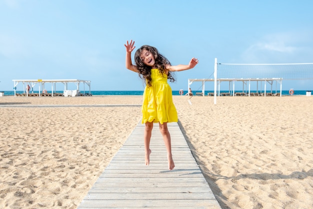 gelukkig krullend meisje dat op een zonnige dag op het zandstrand springt Leuke vakantie Leeg strand Zomer