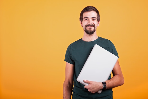 Gelukkig lachend aantrekkelijke man met een laptop in zijn handen geïsoleerd op een oranje achtergrond. Draadloze technologie voor communicatie