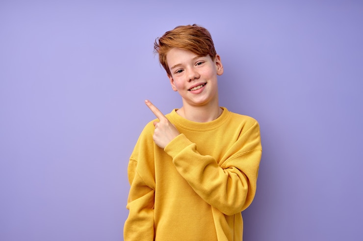 Foto gelukkig lachend aardige jongen in casual gele shirt outfit wijzende wijsvinger aan de zijkant, adviseren, aanbevelen. kopieer ruimte voor advertentie. portret van kaukasische jongen. menselijke emoties, jeugdconcept