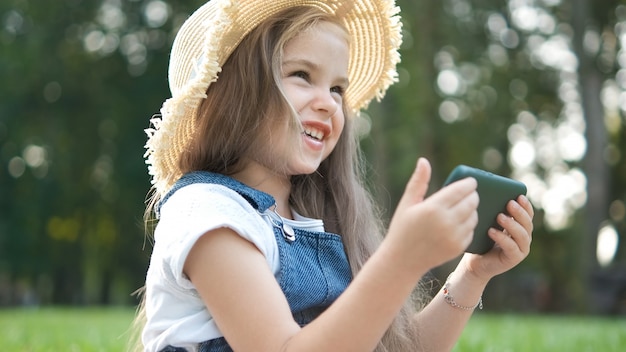 Gelukkig lachend kind meisje kijken in haar mobiele telefoon buiten in de zomer.