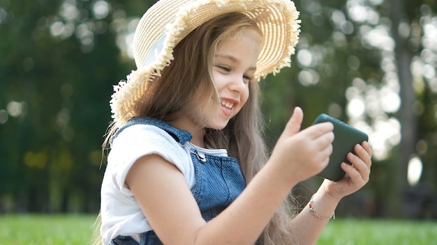 Gelukkig lachend kind meisje op zoek in mobiele telefoon buiten in de zomer.