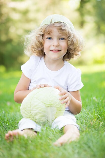 Gelukkig lachend kind met kool zittend op groen gras in het voorjaarspark gezonde levensstijl concept