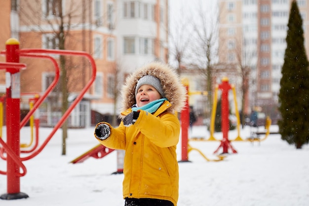 Gelukkig lachend kind met plezier in de sneeuw in de stad Winterpret buiten Jongen in feloranje winterjas Besneeuwde dagen winterpret Wintervakantie