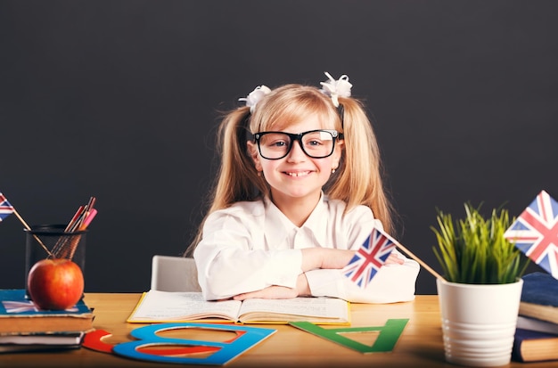 Gelukkig lachend meisje dat Engelstalige werktafel leert met boeken, letters en vlag