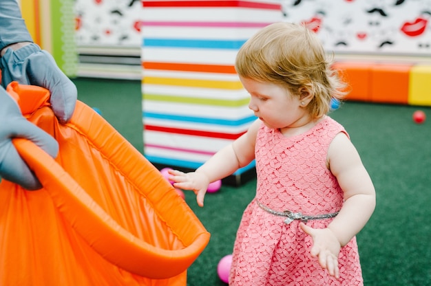 Gelukkig lachend meisje dat speelt met speelgoed, kleurrijke ballen in de speeltuin in de speelkamer. Klein schattig leuk kind op verjaardagsfeestje in kinderpretpark en speelcentrum binnen.