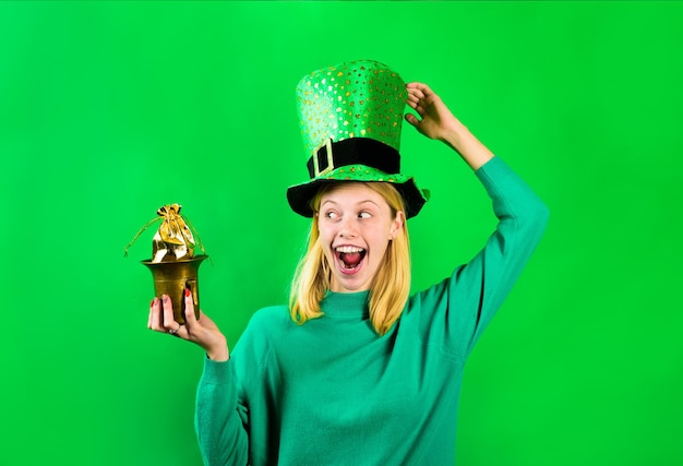 Gelukkig lachend meisje in Leprechaun kostuum houdt pot met goud. Groene hoed. Leprechaun houdt pot met goud vast. Groene kabouter. Hoed met klaver. Sint Patrick's Day. Ierse tradities. Sint patrick.