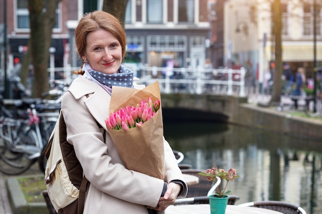 Foto gelukkig lachend meisje met een boeket tulpen staande op een straat van amsterdam. nederland