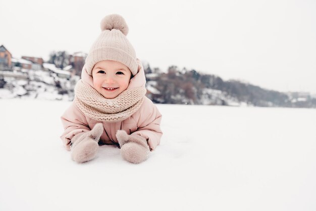 Gelukkig lachend meisje met een roze jas, sjaal en muts, spelend in een prachtige besneeuwde winterwandeling Meisje geniet van een ijzige winterdag Spelen met sneeuw op wintervakantie Wintervakantie concept